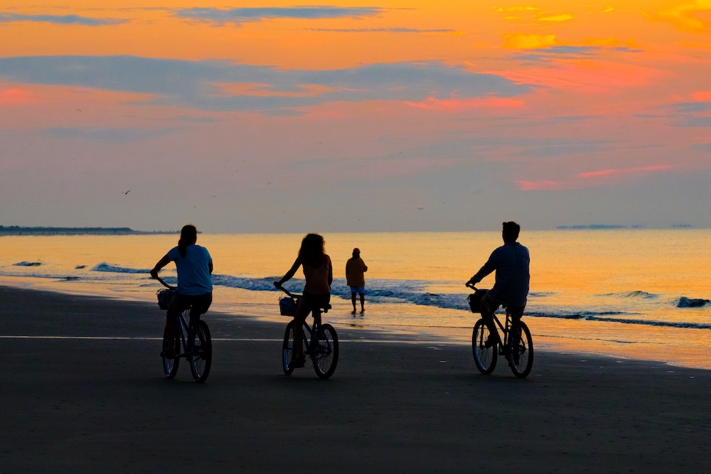 people riding bikes on the beach at sunset low tide