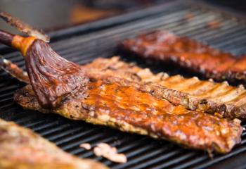 Close up of slabs of barbecue ribs cooking on a large outdoor grill.